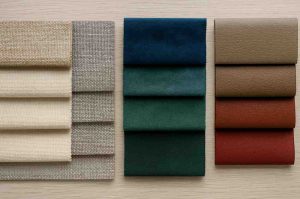 Assorted upholstery fabric samples in neutral, green, and brown shades displayed on a wooden surface – representing fabric options for furniture upholstery