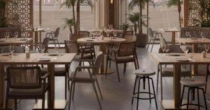 Modern indoor restaurant dining area with wooden tables, mixed chairs, and decorative plants arranged in a stylish, contemporary setting.