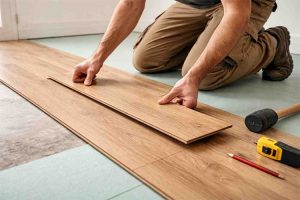 Technician installing laminate wood flooring planks over underlayment during home flooring installation