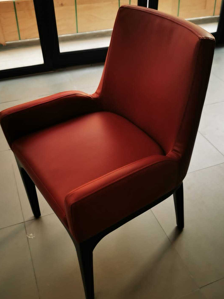 A modern armchair with reddish-brown leather upholstery and dark tapered wooden legs