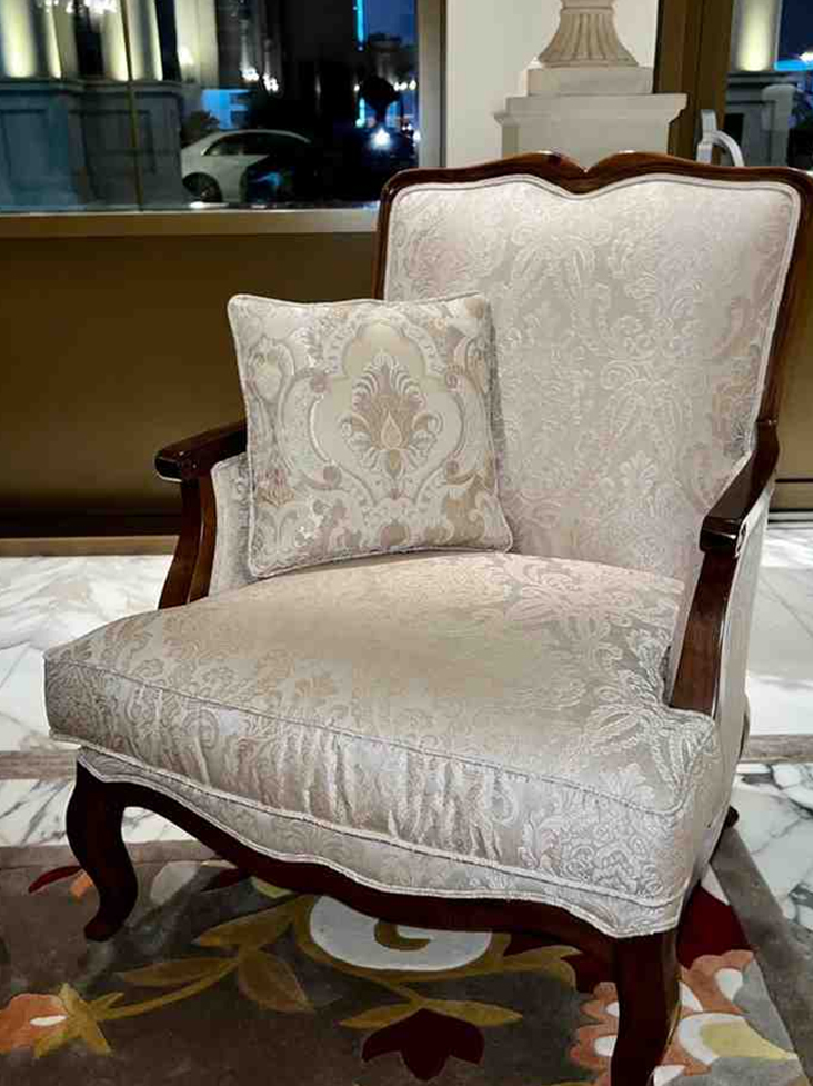 Elegant upholstered accent chair with wooden arms and decorative cushion
