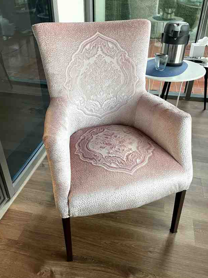 A pink-hued armchair featuring ornate damask patterns on the backrest and seat cushion.