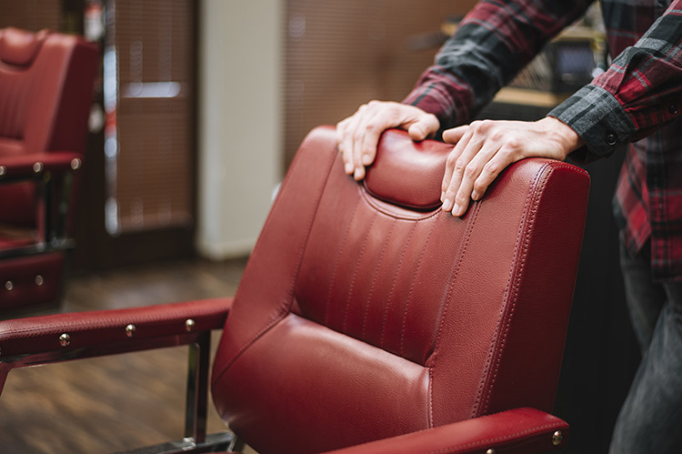 Hands adjusting a red leather recliner chair, showcasing upholstery repair and cushioning detail